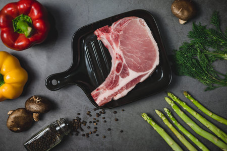 Top view of raw pork for prepare steak surrounded by organic vegetable ingredients.