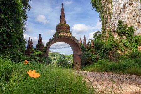 The scenery of the Khao Na Nai Luang Dharma Park or Phutthawadee arch with beautiful orange flowers and green grass foreground in a beautiful clear sky day at Surat Thani Province, Thailand.の写真素材