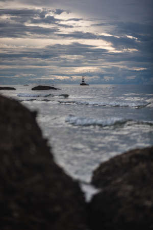 The scenery of the sea and wave with a faraway lighthouse on a cloudy day at Pattaya beach, Thailand.の写真素材