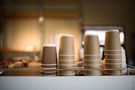 Degradable coffee paper glasses are standing on the top of the coffee machine in a cozy coffee shop.の写真素材