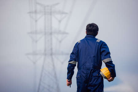 A male power engineer in a yellow helmet inspects the power line under a high voltage electrical line.の写真素材