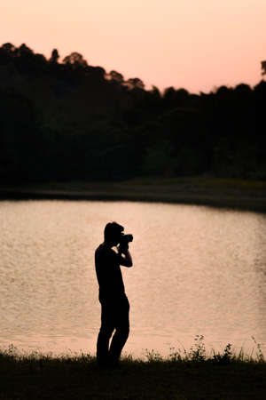Silhouette view of a man taking a photo at the lake in pine tree forest.の写真素材