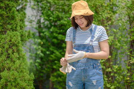 An Asian woman gardener is taking off her gloves after finishing her work.の写真素材