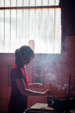 An Asian woman lighting incense sticks to pay homage to the Chinese New Year.の写真素材