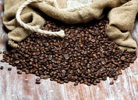 roasted coffee beans spilled out of the bag on a wooden tableの写真素材
