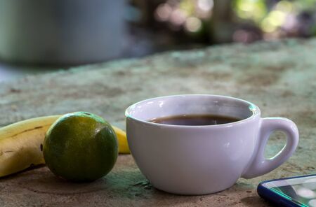 A cup of coffee and fruits on a concrete table in natural background. Take a break for drinking and relax during outdoor working.の写真素材