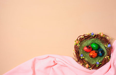 Colorful painted quail eggs in a nest on a beige background and pink fabric. Easter table. Copy...