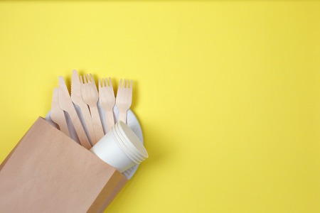Eco-friendly disposable utensils made of bamboo wood and paper in paper bag on yellow background. Go green, save environment concept - Imageの写真素材