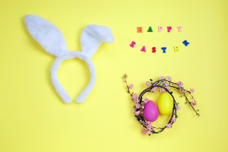 Happy easter with adorable bunny ears on a bird nest with colorful eggs against on yellow background. Flat layの写真素材