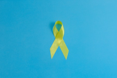 Yellow ribbon on blue bakground - bladder, liver and bone cancer awareness symbol. Support our troops concept. Isolated background, copy space, close up, top view, flat layの写真素材