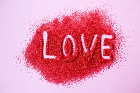 Word LOVE written by hand in red sugar on pink background. Wishes for Valentine's Day. Declaration of love.の写真素材