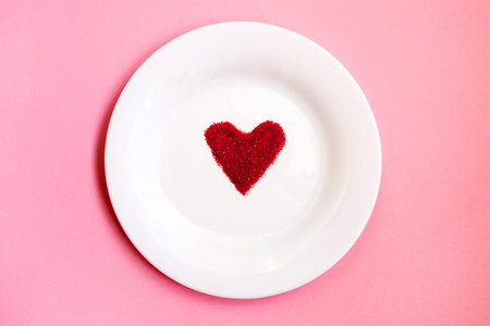 Festive table setting for Valentine's Day. Red sugar heart on a white plate on a pink background ....