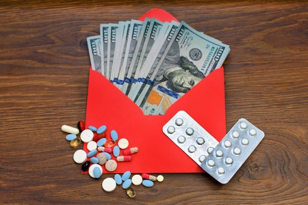 dollars currency in the envelope against scattered tablets, pills, capsules. Medical expenses, purchase of medications. medicine concept.の写真素材