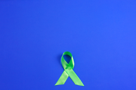 Light green ribbon on blue background. Liver Cancer Lymphoma Awareness. Mental health awareness. Healthcare and medicine concept.の写真素材