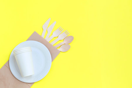 Eco-friendly disposable utensils made of bamboo wood on paper bag on yellow background. Draped...