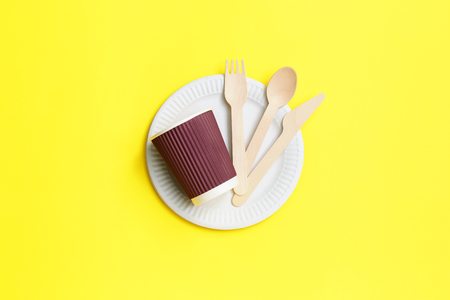 Disposable tableware from natural materials, wooden spoon, fork, knive, paper bowl with paper cup on yellow background. eco-friendly. Concept of disposable tablewareの写真素材