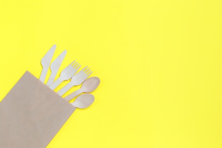 Disposable tableware from natural materials, wooden spoons, knives, and forks in paper bag on yellow background. eco-friendly. Concept of disposable tableware. Copy spaceの写真素材