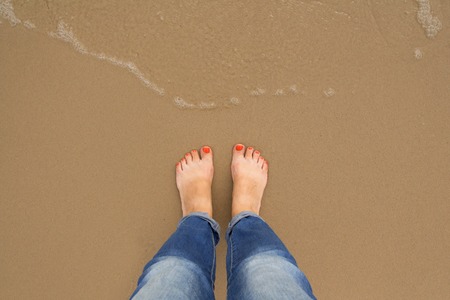 Orange nail pedicure Feet of female stand on the summer sand beach, top view, Woman solo travel concept. Vacation concept,の写真素材