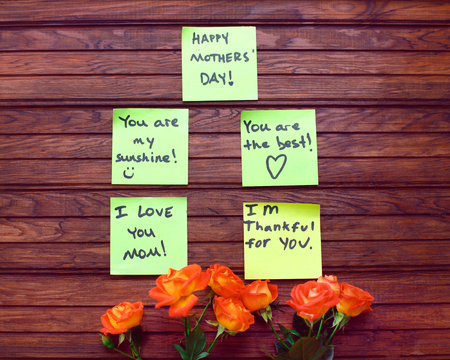 Happy Mother's Day note reminder yellow sticker and beautiful fresh vivid orange roses tinged with red on on wooden background, close up. Festive concept. LOVE MOM messageの写真素材