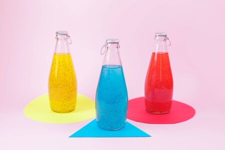 Summer multicolored refreshing drink in the bottles with basil seed and fruit juice on pink background. Exotic healthy beverage.の写真素材