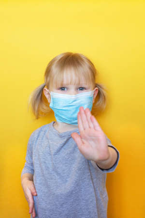 Cute little girl wearing a protective mask holding toilet paper roll on her head. Funny, positive photo. Corona virus scare. Epidemic Precautions. The child is in quarantine.の写真素材