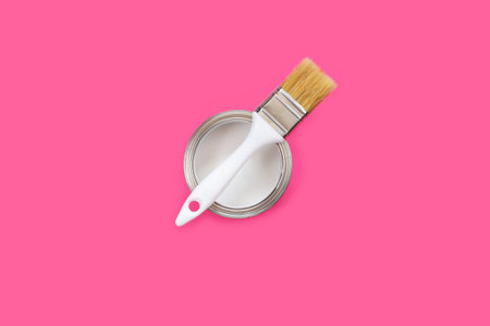 Open can with white paint and brush on color pink background. Sunny summer. Bright Sweet fashion Style. Minimal Fun. Top view. Renovation concept.の写真素材