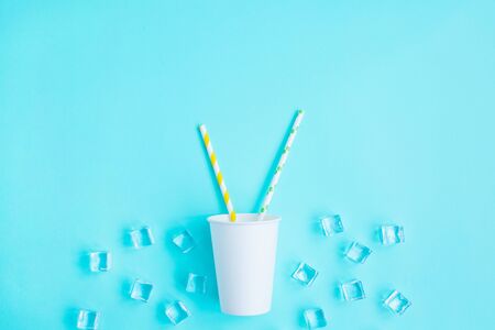 White paper caps with color cocktail straw and ice on blue background. Space for text. recycling eco concept. pop art style. Partyの写真素材