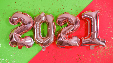 Foil balloons in the form of numbers 2021 on green and red background and confetti. Flat lay. New year celebration. Holiday party decoration.の写真素材