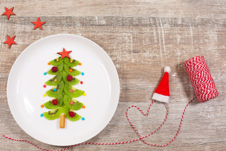 Christmas tree made of kiwi slices on wooden table. Creative idea for Christmas breakfast or New Year festive desserts for kids. Top view.の写真素材