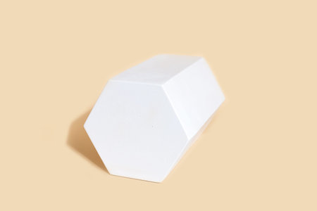 Hexaconal prism geometric figure in white color that casts shape on pastel beige color background....