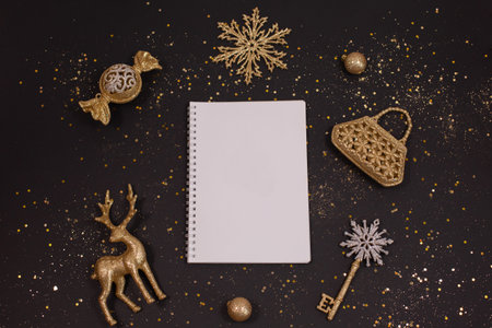 Holiday golden decorations and white notebook on black background. Christmas planning concept. Flat lay style.の写真素材
