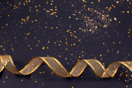 Close up of festive gold bronze metallic ribbon on black glitter backgroundの写真素材