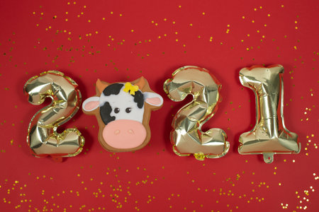Gingerbread bull and Foil balloons in the form of numbers 2021 on red background .. Christmas, happy new year 2021. New year's food. Space for textの写真素材