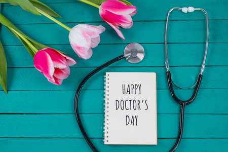 Pink tulips and stethoscope with spiral notepad with Happy Doctors Day text on it.の写真素材