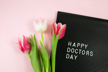Black letterboard with white plastic letters with quote Happy Doctors day and Bunch of pink tulips...