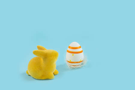 Yellow Easter bunny rabbit with painted egg on blue background.の写真素材