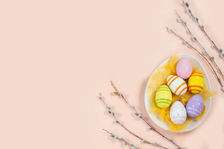 Easter colorful eggs in an egg-shaped plate with willow twigs on light background.