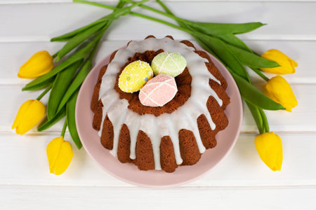 Glazed easter cake decorated with mini eggs candy and yellow tulips