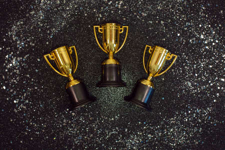 Golden winner cups with silver sparkles on a black background.の写真素材