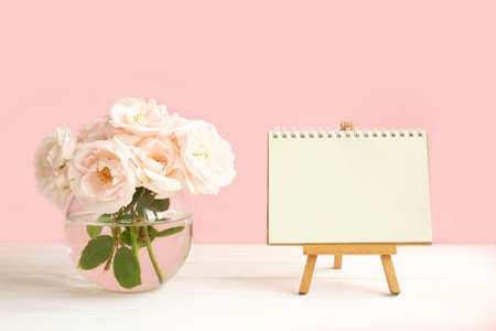 Tender pink garden roses in a transparent vase and an Easel with blank notebook paper for writing wishes.の写真素材