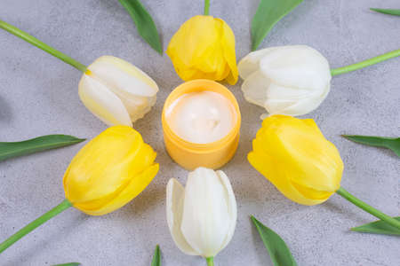 Spa concept cream in a glass jar for cream around tulips flowerの写真素材