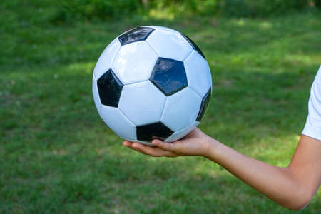 Soccer ball white and black leather in hand of football player on green grass.の写真素材