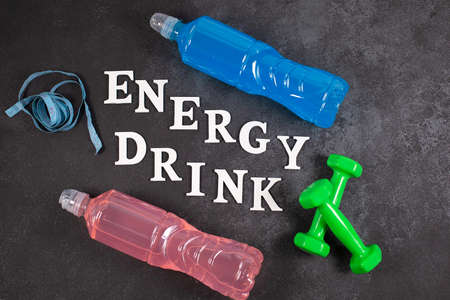 Words ENERGY DRINK and Bottles with different flavors and dumbbells on a dark background. Sport beverage.の写真素材
