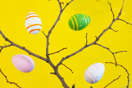 Branch of tree and colorful Easter eggs on a yellow background.