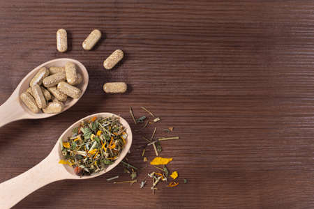 Organic pills on wooden spoon wiht herbals on wooden background.の写真素材