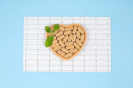 Herbal pills in heart shaped wooden plate and cardiogram on blue background.の写真素材
