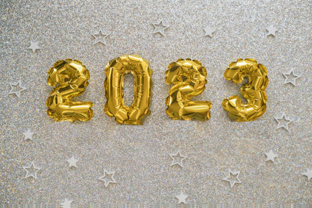 2023 gold foil balloons and confetti on silver glitter background.