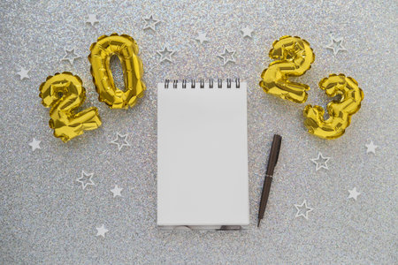 2023 gold foil balloons and notebook with a pen on Christmas background
