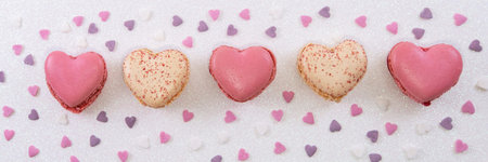 Sweet macaroons in heart shape and colorful confetti on white glitter background.