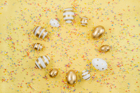 Easter gold eggs with Colorful Confetti scattered on yellow background.の写真素材